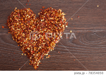Red hot chili pepper flakes lying on wooden table in heart shape. Cooking concept, seasonings for food. Red hot chili pepper flakes lying on wooden table in heart shape. Cooking concept, seasonings for food. 78354050