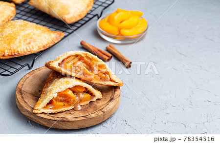 Small peach and cinnamon hand pies with crust dough,  sprinkled with sugar, on wooden plate and cooling rack, horizontal, copy space 78354516