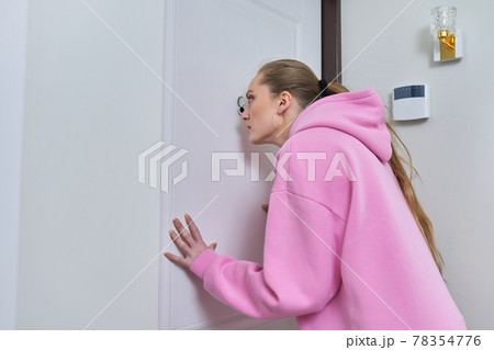 Young woman looking through peephole of front door in apartment. Young woman looking through peephole of front door in apartment. 78354776