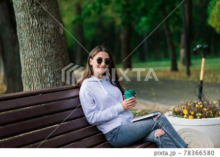 Young woman riding scooter in park sitting on bench Young woman riding scooter in park sitting on bench 78366580