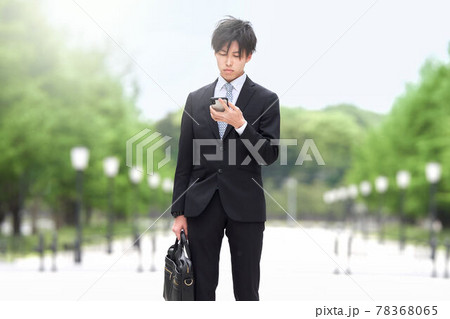 立ち止まってスマホを見る若いビジネスマン 立ち止まってスマホを見る若いビジネスマン 78368065