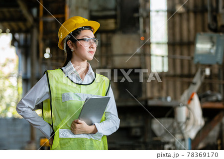 Woman engineer industry heavy worker wearing hardhat and holding tablet standing at machine area. 78369170