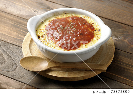 鍋敷きに置かれた溶けて焦げ目がついたたっぷりチーズの熱々ドリア、グラタンと木製のスプーン 78372306