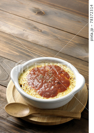 鍋敷きに置かれた溶けて焦げ目がついたたっぷりチーズの熱々ドリア、グラタンと木製のスプーン 鍋敷きに置かれた溶けて焦げ目がついたたっぷりチーズの熱々ドリア、グラタンと木製のスプーン 78372314