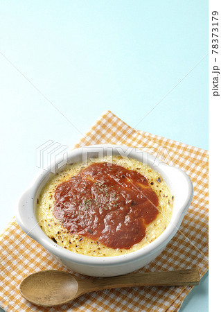 ランチョンマットと耐熱皿に入った溶けて焦げ目がついたたっぷりチーズのドリア、グラタンと木製のスプーン 78373179