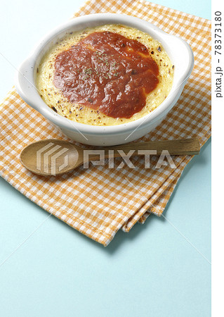 ランチョンマットと耐熱皿に入った溶けて焦げ目がついたたっぷりチーズのドリア、グラタンと木製のスプーン 78373180