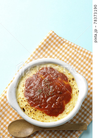 ランチョンマットと耐熱皿の中の溶けて焦げ目がついたたっぷりチーズのドリアと木製のスプーンを俯瞰で撮影 78373190