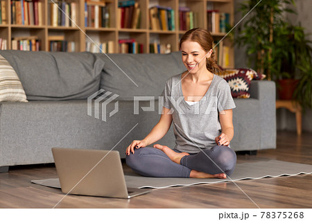 Young happy woman having online yoga class on laptop at home, sitting in lotus pose on floor Young happy woman having online yoga class on laptop at home, sitting in lotus pose on floor 78375268