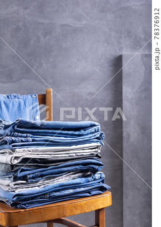 Denim jeans at old wooden chair near grey wall background texture.  Stack of jeans 78376912