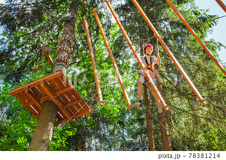 Teen boy on a ropes course in a treetop adventure park passing hanging rope obstacle 78381214