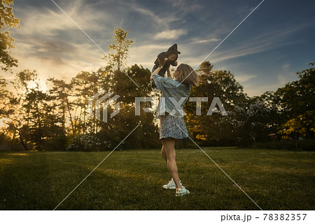 Mother throws baby up, playing and laughing in sun summer day on nature. Happy family outdoors. 78382357