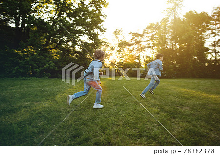 Two brother boys running outdoors in park at sunset time 78382378
