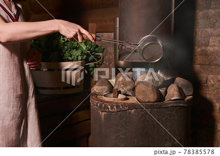 woman in a bath pours water on hot stones on the stove 78385578