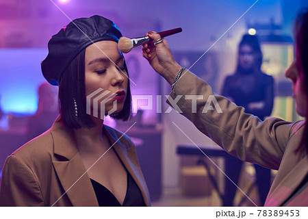 Make-up artist applying powder on face of young female musician Make-up artist applying powder on face of young female musician 78389453