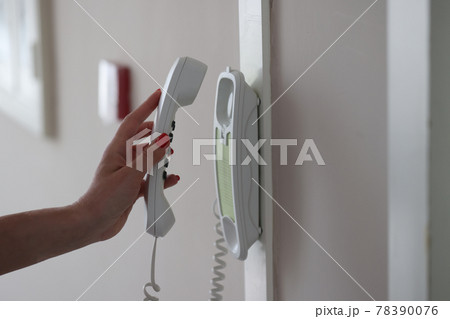 Woman hand picks up intercom receiver in apartment Woman hand picks up intercom receiver in apartment 78390076
