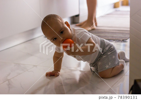 Sweet little baby with ball in his mouth crawling on the kitchen floor Sweet little baby with ball in his mouth crawling on the kitchen floor 78390131