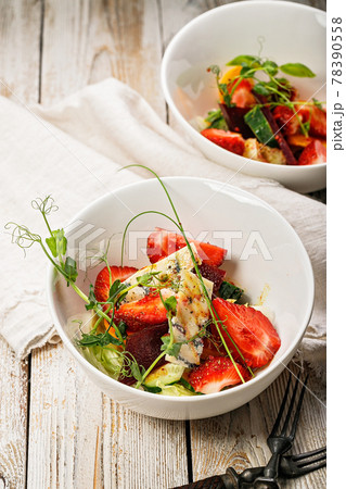 Vertical shot delicious summer salad. Salad with fresh strawberries, baked beets, yellow tomatoes, dor blue cheese and herbs in a white bowl on a light rustic background. Summerfood. Close-up Vertical shot delicious summer salad. Salad with fresh strawberries, baked beets, yellow tomatoes, dor blue cheese and herbs in a white bowl on a light rustic background. Summerfood. Close-up 78390558