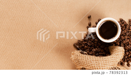 Hot coffee cup and coffee beans on brown background top view Hot coffee cup and coffee beans on brown background top view 78392313