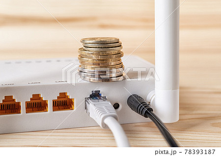 Stack of coins on the white Wi-Fi wireless router with connected cables on a wooden desk. 78393187