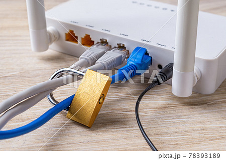 Locked padlock on network cables connected to white Wi-Fi wireless router on a desk. 78393189