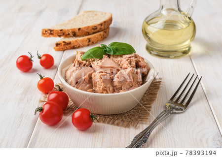 Canned tuna meat in a bowl, fork, bread and fresh red cherry tomatoes on a white wooden table. Canned tuna meat in a bowl, fork, bread and fresh red cherry tomatoes on a white wooden table. 78393194