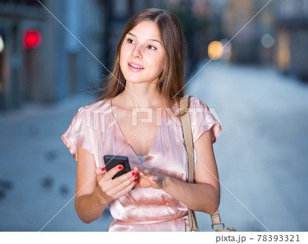 woman looking to phone in hands and chatting in city 78393321