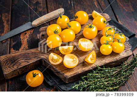 Yellow cherry tomato sliced on a wooden cutting board. Dark wooden background. Top view 78399309