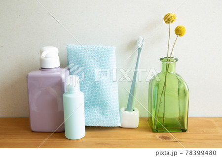 Bathroom bottles, shower towel, toothbrush, vase of plant on wooden table. white wall background. Skin care and spa concept Bathroom bottles, shower towel, toothbrush, vase of plant on wooden table. white wall background. Skin care and spa concept 78399480