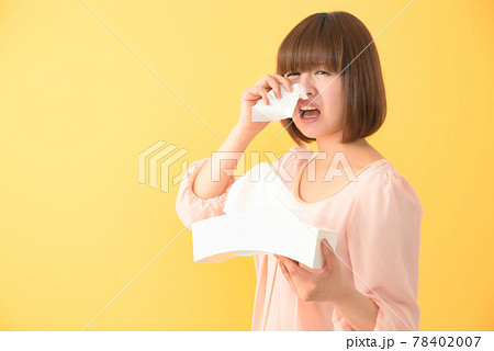 ティッシュボックスを持ちながらつらそうな顔で鼻をかむ若い女性 78402007