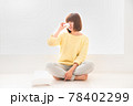 床に座りティッシュで鼻を抑える辛そうな顔の若い女性 78402299