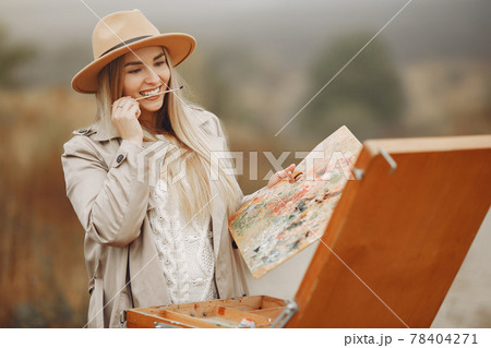 Woman in a brown coat painting in a field 78404271