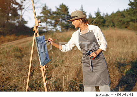 Woman in a apron painting in a field Woman in a apron painting in a field 78404541