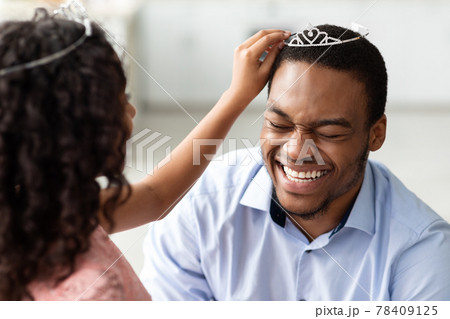 Curly little girl putting crown on her laughing father Curly little girl putting crown on her laughing father 78409125