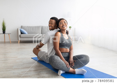 Smiling African American couple relaxing after yoga practice, sitting on fitness mat back to back, smiling at camera 78409581