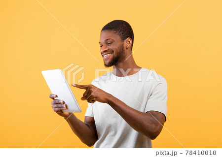 African american male blogger using digital tablet, surfing in internet, isolated on yellow background, studio shot 78410010