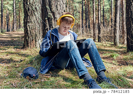 Young artist sits in pine forest and plein air painting and listens to music. Sunny day, creative leisure 78412185