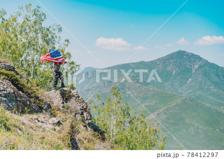 On rock, man in military uniform holding an American flag On rock, man in military uniform holding an American flag 78412297