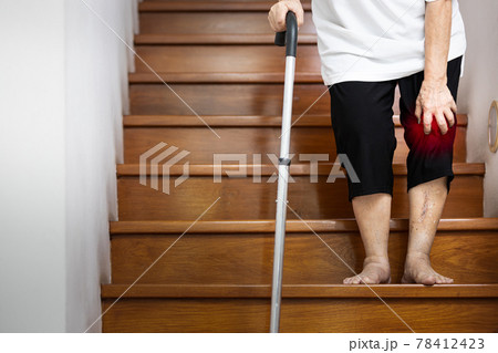 Hand of female elderly holding her pain knee with hand and walking stick for support when walking,old age has an injury,painful in the joint and bone in her knee,symptoms of Osteoarthritis,Arthritis 78412423