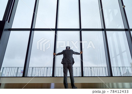 窓に手をついて下を向くビジネスマンの後ろ姿 78412433