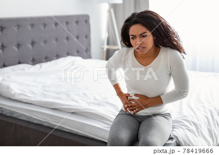 Woman with right side pain sitting on bed at home 78419666