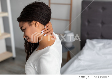 Portrait of black woman with neck pain sitting on bed 78419667