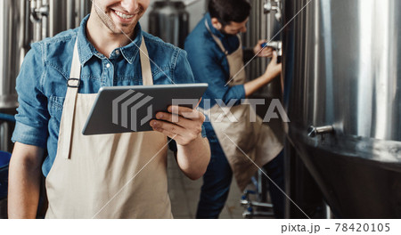 Beer production process at brewery. Man operating brewing equipment at beer making factory and using digital tablet 78420105