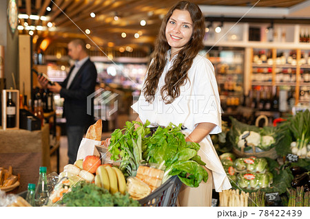 Positive young woman with shopping cart at supermarket 78422439