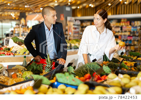 Positive young couple with a grocery cart in the supermarket, choose pears Positive young couple with a grocery cart in the supermarket, choose pears 78422453