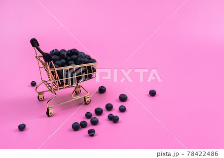 Blueberries in a grocery cart on a pink background. Scattered blueberries near a grocery cart on a pink background. 78422486