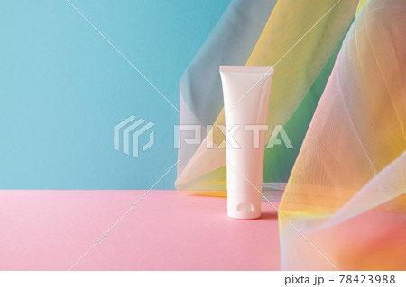 White plastic tube for beauty product on blue pink background with colorful rainbow organza fishnets fabric drapery 78423988