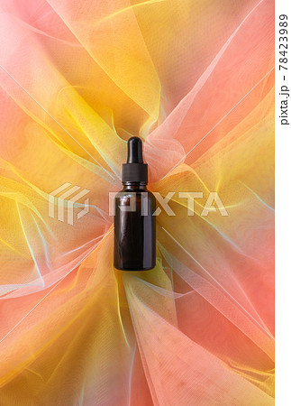 Serum brown glass jar with pipette for beauty product on colorful rainbow organza fabric. Liquid vitamin C facial serum 78423989