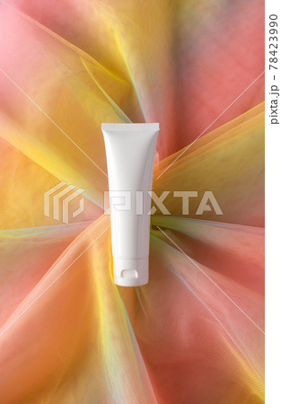 White plastic tube for beauty product on colorful rainbow organza fishnets fabric. Moisturizer cream lotion mockup 78423990