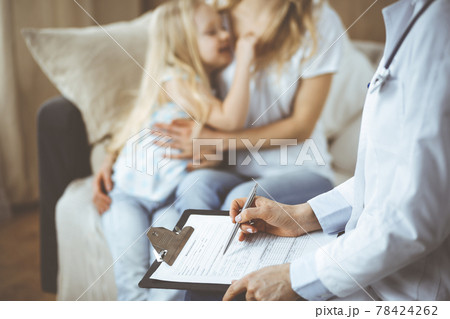 Doctor and patient. Pediatrician using clipboard while examining little girl with her mother at home. Sick and unhappy child at medical exam. Medicine concept Doctor and patient. Pediatrician using clipboard while examining little girl with her mother at home. Sick and unhappy child at medical exam. Medicine concept 78424262