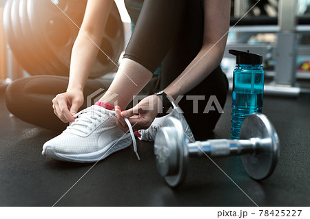 スポーツジムでシューズのヒモを結ぶ若い女性の手元 78425227